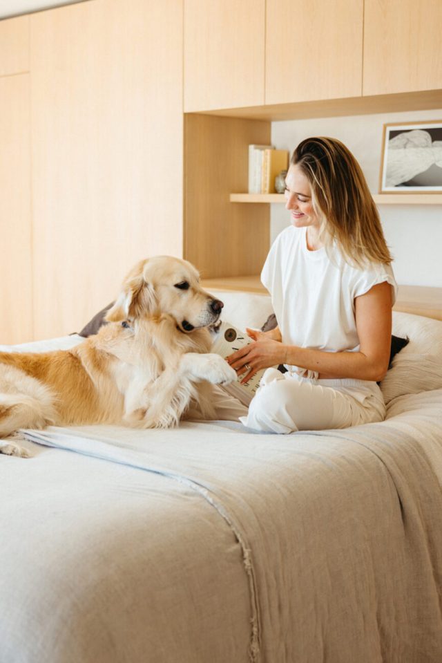 Mulher lendo os melhores livros de autoajuda na cama enquanto acaricia um cachorro.