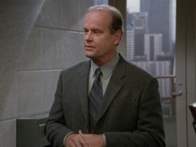 Frasier stands in his apartment wearing a suit