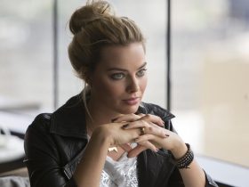 Margot Robbie as Jess sitting at a table in Focus