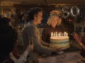 Margaret looking at a lit birthday cake, surrounded by friends in Here