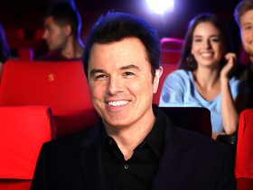 A smiling Seth MacFarlane seated in a movie theater with other scattered audience members behind him