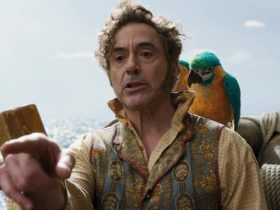 Dr. Dolittle, standing on the deck of a ship, a macaw on his shoulder, pointing at something