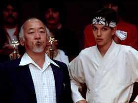 Mr. Miyagi and Daniel standing next to trophies at a karate tournament in The Karate Kid